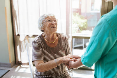 Smiling senior woman holding hands of healthcare worker at nursing home