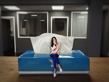 Digital composite image of young woman sitting on tissue paper box at home