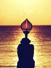 Silhouette cross on beach against sky during sunset