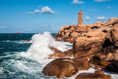 Lighthouse by sea against cloudy sky