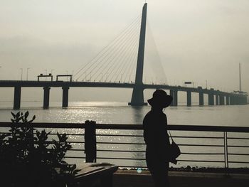 Rear view of silhouette man walking on suspension bridge