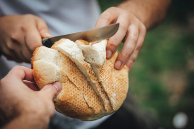 Cropped hands of people cutting bread outdoors