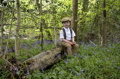 Portrait of cute boy sitting on log in forest