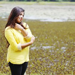 Young woman standing on field by lake