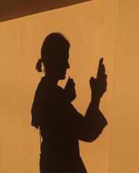 Shadow of woman using mobile phone on orange wall