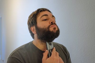 Young man shaving beard at home