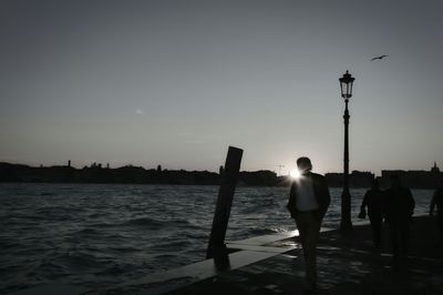 Woman standing by sea against sky at sunset