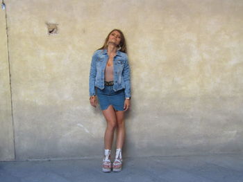 Full length portrait of woman standing against wall