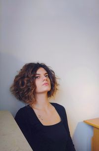 Thoughtful young woman looking away while sitting against wall at home