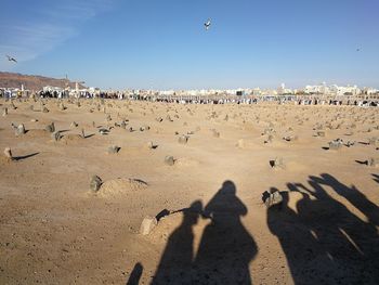 Shadow of people on sand in cemetery against sky