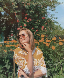 Young woman wearing sunglasses standing against plants