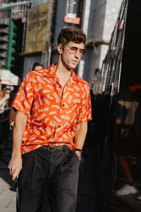 Young man looking away while standing on street in city