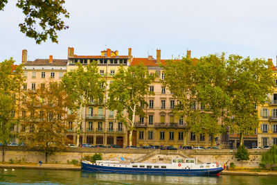 Boats moored in river by buildings against sky