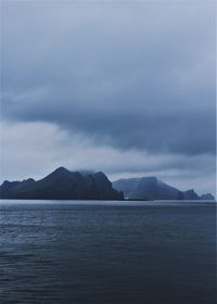 Scenic view of sea by mountain against sky