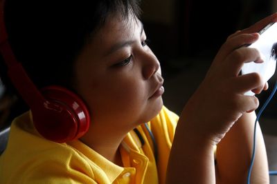 Close-up of boy listening to headphones while using smart phone