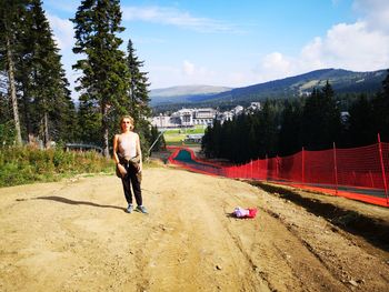 Full length of mature woman walking on dirt road against sky during sunny day