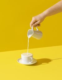 Woman pouring milk from a jug, in bright light, isolated on yellow background. milk dripping.