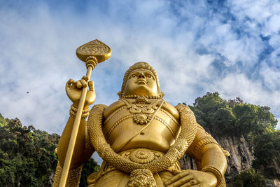 Low angle view of golden statue and trees against cloudy sky