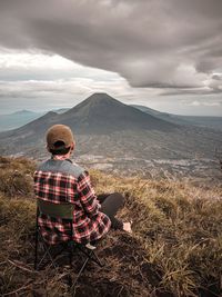 Rear view of woman sitting on mountain against sky