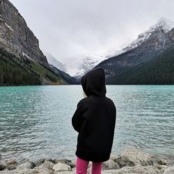 Rear view of girl standing by lake during winter