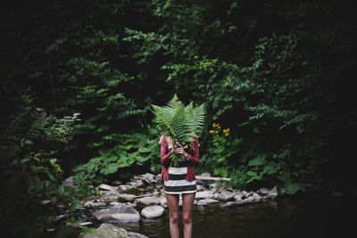 Woman covering face with leaves in forest