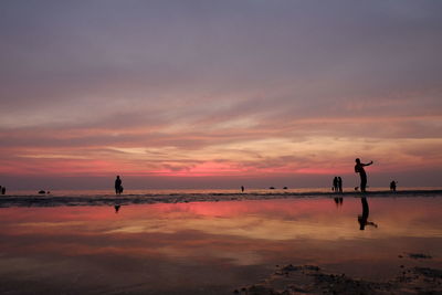 Silhouette people on sea against sky during sunset