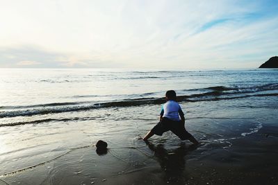 Rear view of woman standing on beach against sky