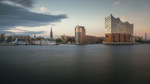 City by river against sky at dusk