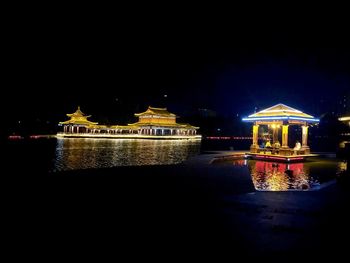 Illuminated building by sea against sky at night