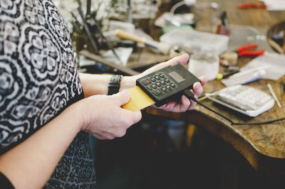 Midsection of woman holding mobile phone on table