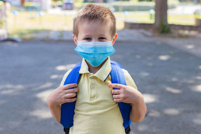 Boy wearing a protective mask with a backpack behind his back in the schoolyard 