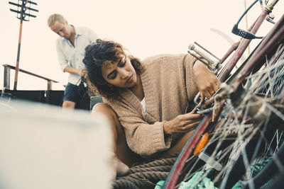 Mid adult woman repairing bicycle while boyfriend in background at houseboat