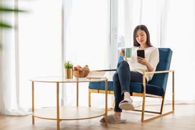 Young woman using phone while sitting on table