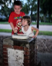 Playful siblings drinking water from faucet at park