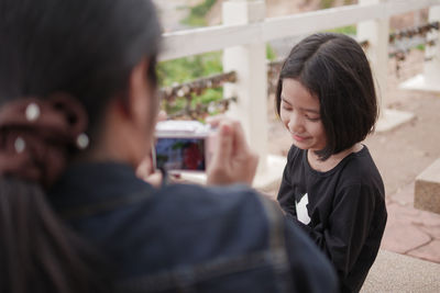 Girl posing for mother photographing with camera on bridge