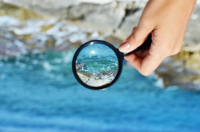 Cropped image of woman's hand holding magnifying glass over sea waves