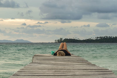 Woman sitting on pier over sea against sky