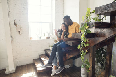 Smiling young couple sitting on stairs in a loft sharing cell phone