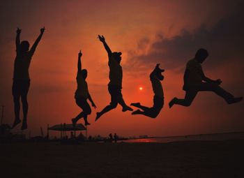 Silhouette of people jumping on beach against during sunset