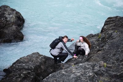 High angle view of father and daughter sitting on rock formation at sea