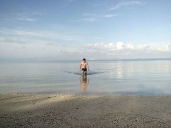 Rear view of man standing on beach against sky