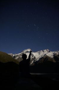 Rear view of man sitting against mountain range at night