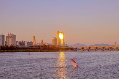 Sailboats in sea against buildings during sunset