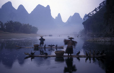 Blurred motion of people on boat in river with reflection against mountains