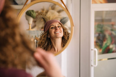 Woman fashion designer joyfully smiles as she adjusts her stylish headband in a mirror