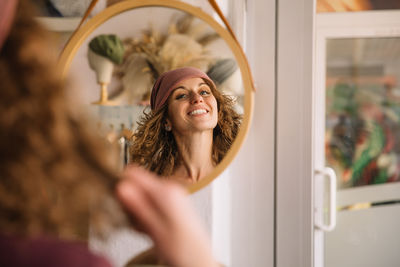 Woman fashion designer joyfully smiles as she adjusts her stylish headband in a mirror