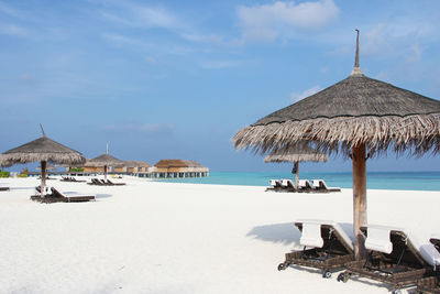 Lounge chairs and parasols on beach against sky