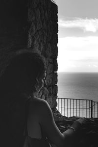 Rear view of woman looking at sea leaning against an ancient wall