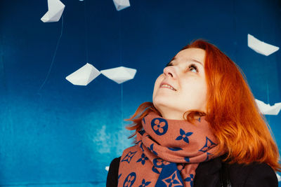 Smiling woman looking at paper boats hanging against blue wall