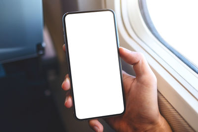 Cropped hand of man holding blank mobile phone in airplane